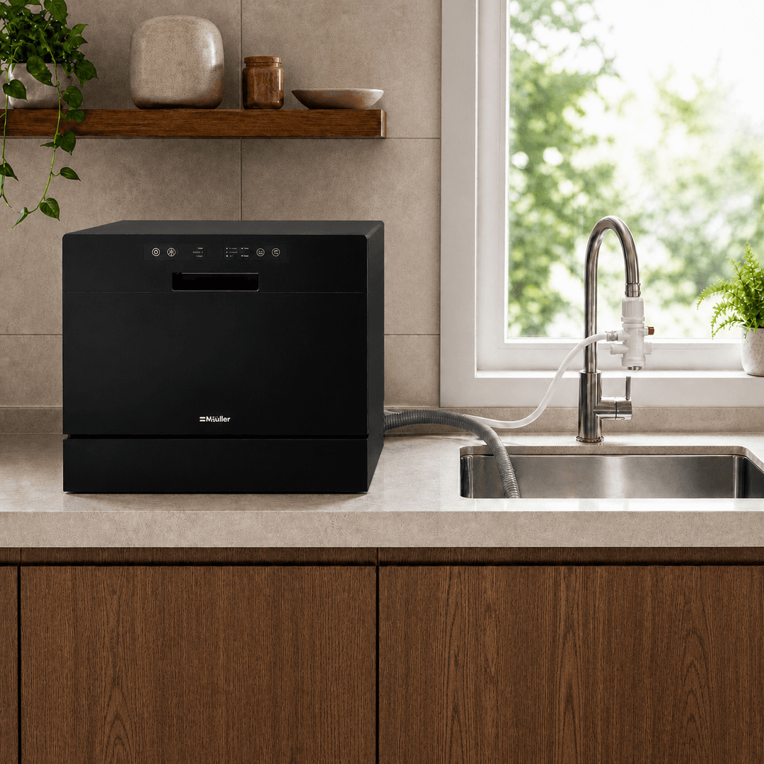 Black countertop dishwasher with white water connection hose linked to faucet and another grey hose from the back of the dishwasher that drains into the sink next to the dishwasher. Modern kitchen setting with brown cabinets and shelf overhead. Dishwasher is on the countertop.