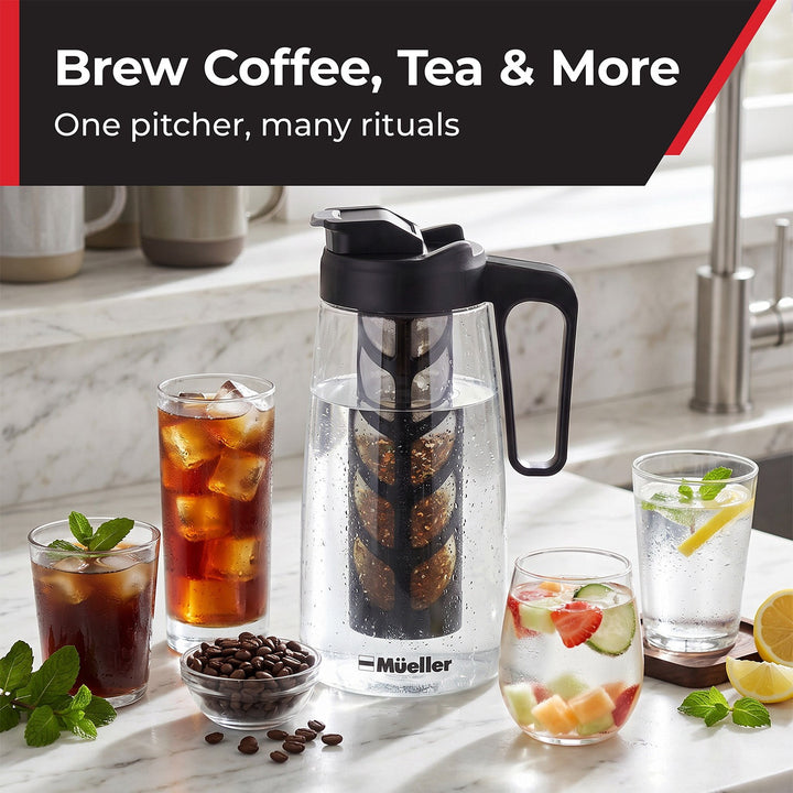 A Mueller coffee infuser pitcher with a black handle and lid sits on a marble countertop in a kitchen setting, surrounded by glasses of iced coffee, tea, and fruit water, with a bowl of coffee beans.