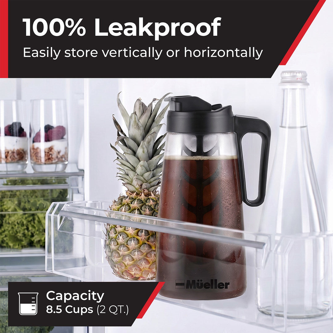 A clear plastic refrigerator storage tray holding a Mueller cold brew pitcher filled with dark coffee, next to a pineapple and a clear bottle.