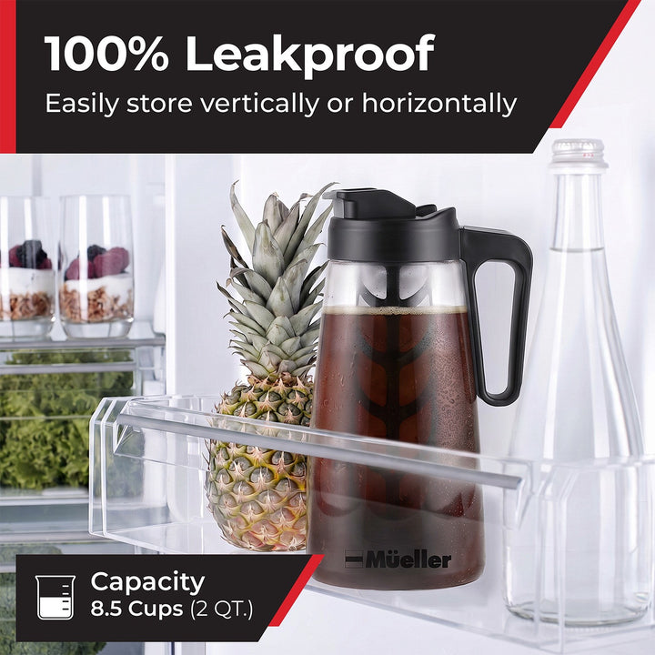 A clear plastic refrigerator storage tray holding a Mueller cold brew pitcher filled with dark coffee, next to a pineapple and a clear bottle.