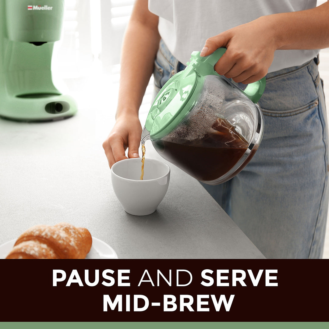 Person pouring coffee from a spearmint green coffee maker into a white cup on a kitchen counter.
