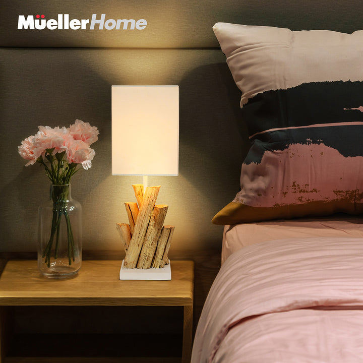 Bedroom scene with a lamp, vase of flowers, and bed with striped pillows.