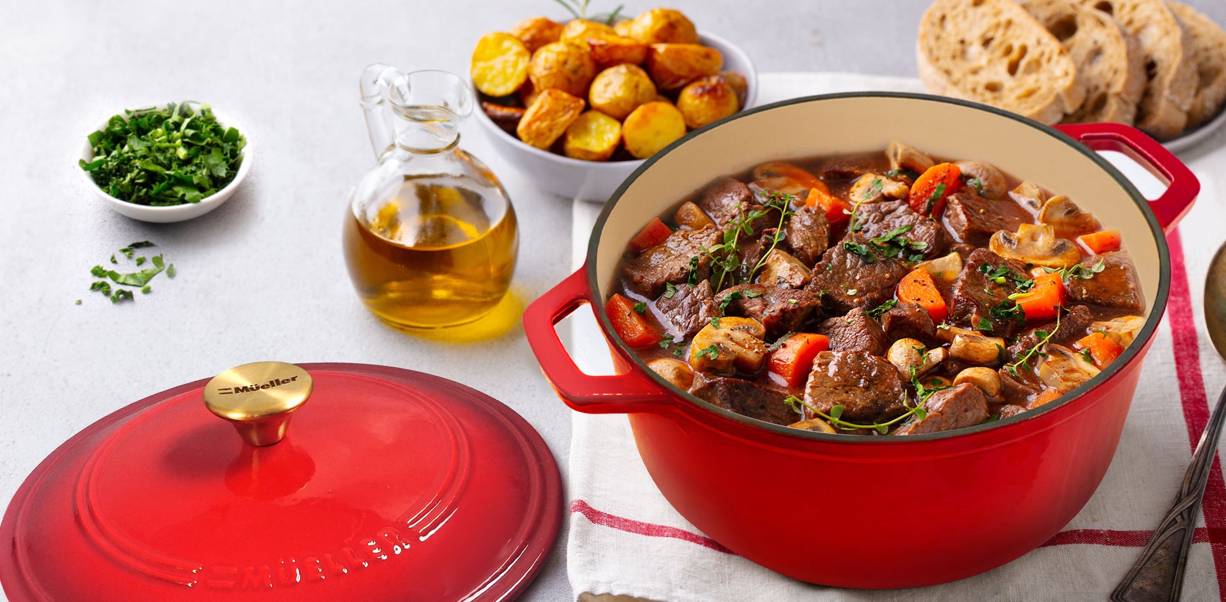Red Mueller Dutch Oven with beef stew on a table with vegetables and bread