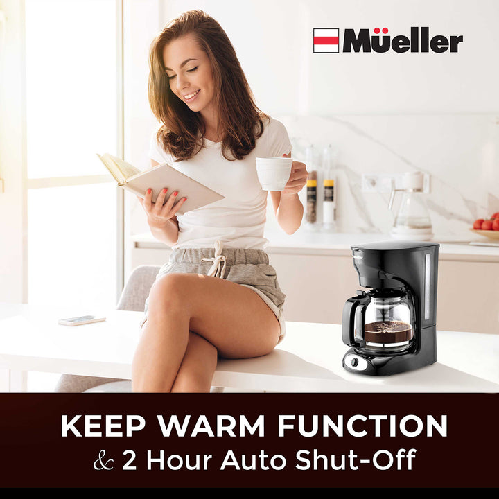 Woman reading a book and holding a coffee cup in a kitchen with a Mueller coffee maker.