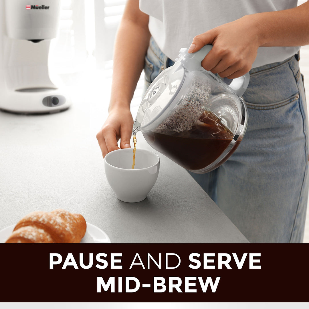 Person pouring coffee from a glass carafe into a white cup on a kitchen counter emphasis on the pause and swerve mid-brew option.