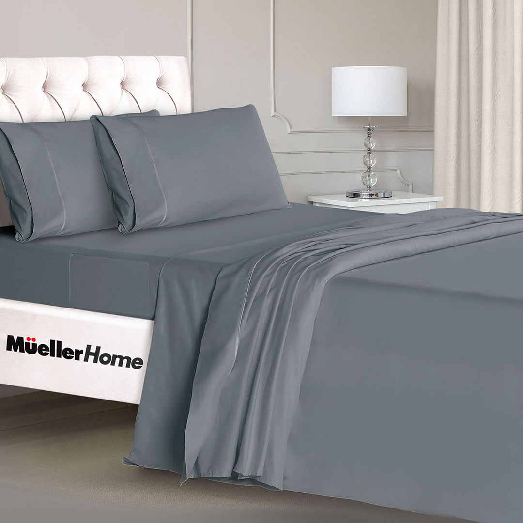 Gray bedding set on a bed with a nightstand and lamp in the background, featuring the Mueller Home logo.
