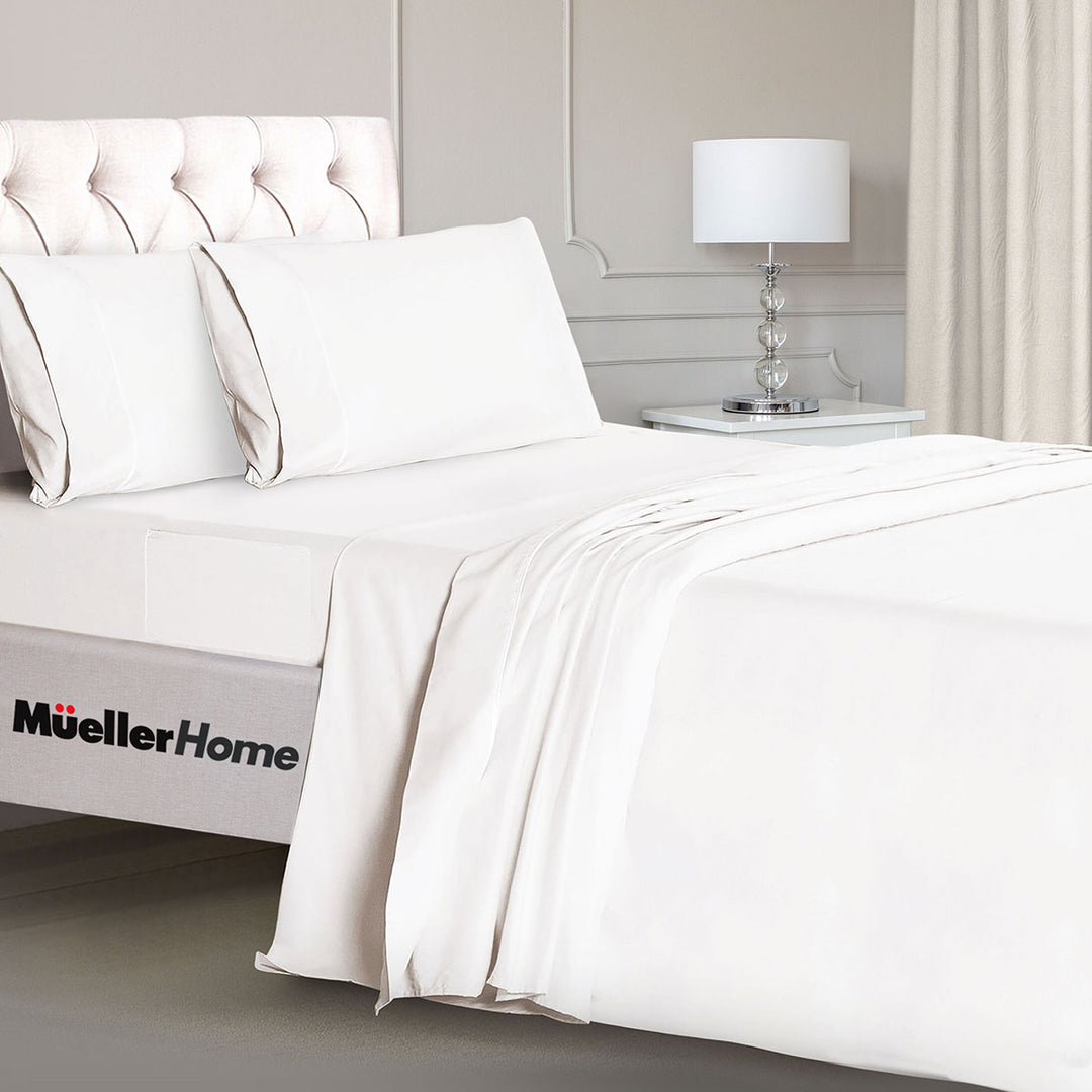 White bedding set on a bed with a lamp in the background, featuring the Mueller Home logo.