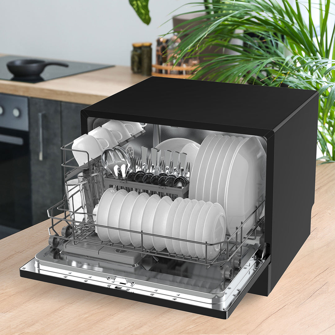 Black compact dishwasher with dishes inside on a kitchen counter.