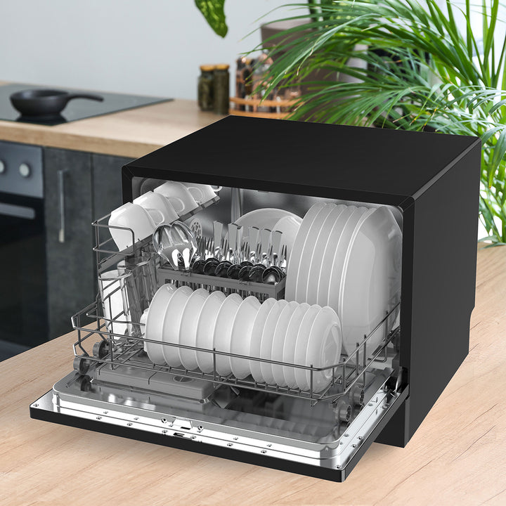 Black compact dishwasher with dishes inside on a kitchen counter.