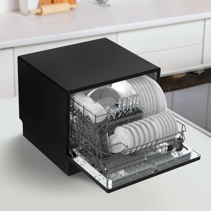 Black compact dishwasher with dishes inside on a kitchen counter.