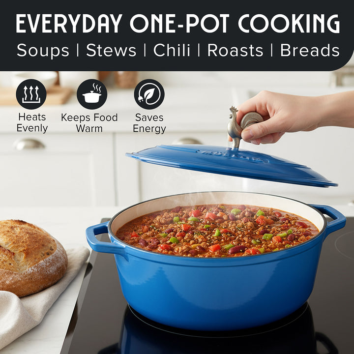 Mueller Enameled Dutch Oven Aqua Blue oval shaped with chili cooking on a stove, surrounded by bread and kitchen items.
