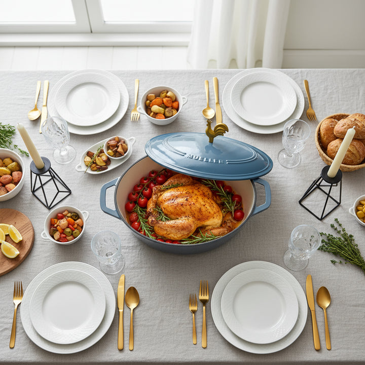 Dining table set with roasted chicken in a blue Dutch Oven Mueller casserole dish, surrounded by plates, utensils, and side dishes.