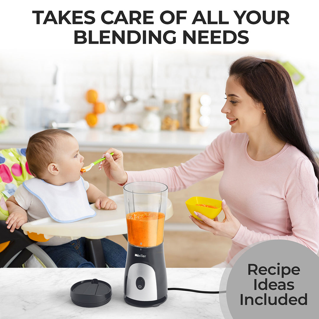 Woman feeding a baby with a spoon next to a blender on a kitchen counter.