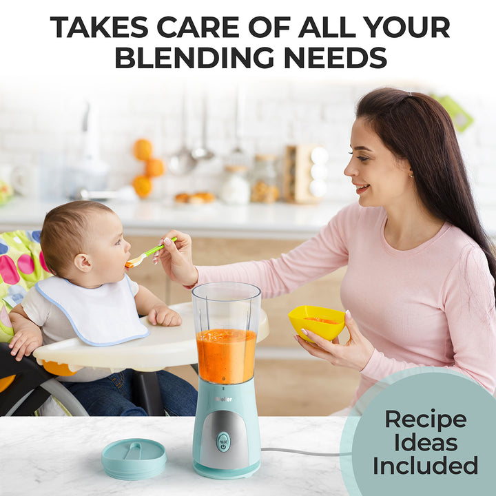 Woman feeding a baby with a spoon next to a blender in a kitchen setting