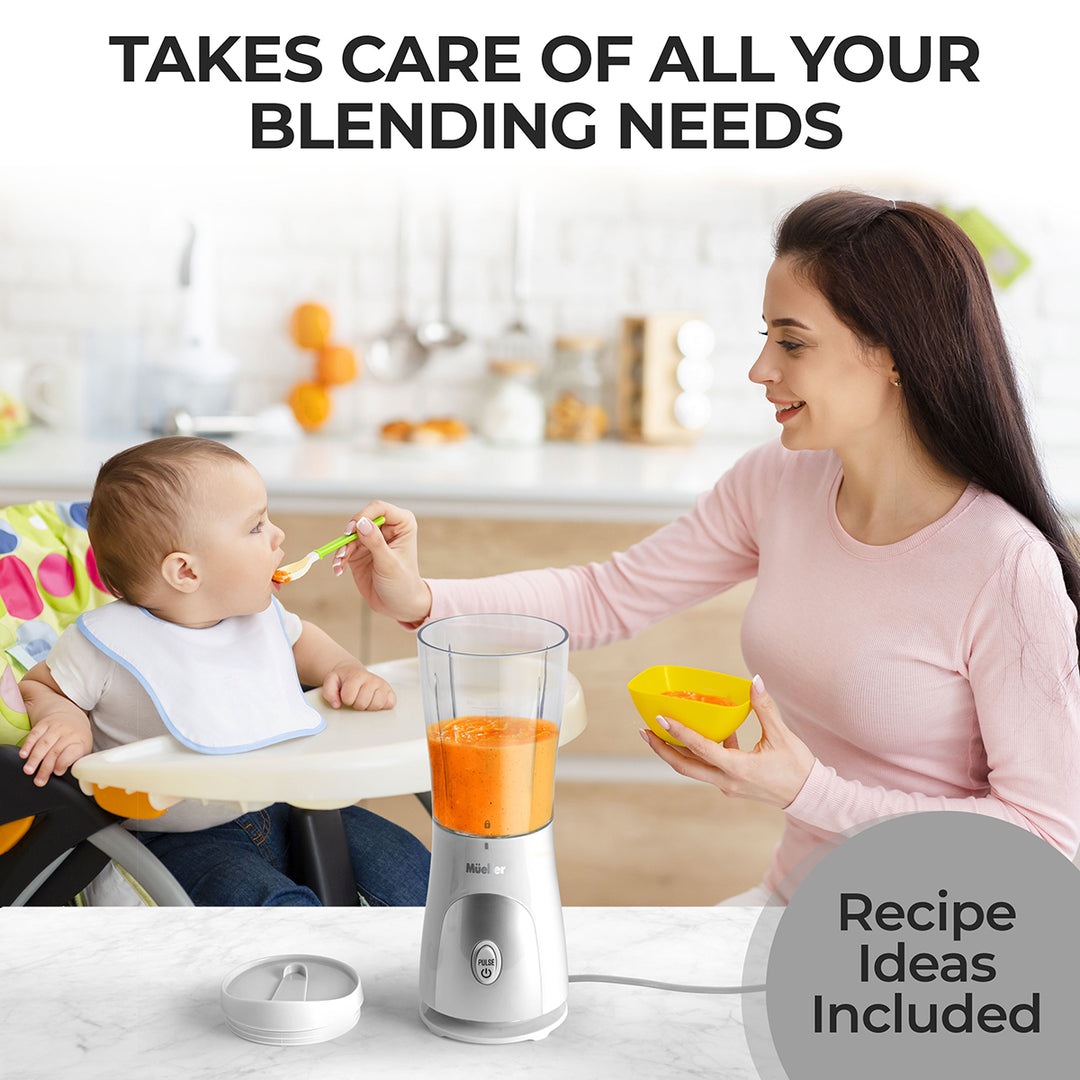 Woman feeding a baby with a spoon next to a blender on a kitchen counter.