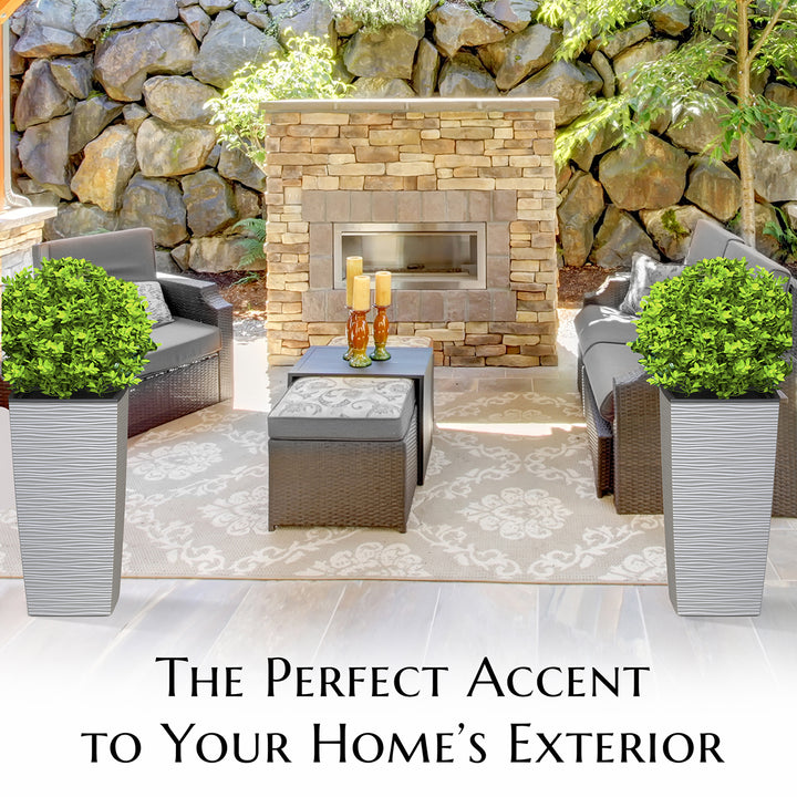 Outdoor patio with stone fireplace, chairs, and plants against a stone wall.