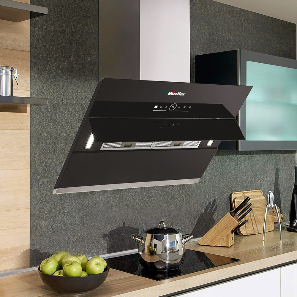 Modern kitchen with a black range hood, silver pot, and green apples on a counter.