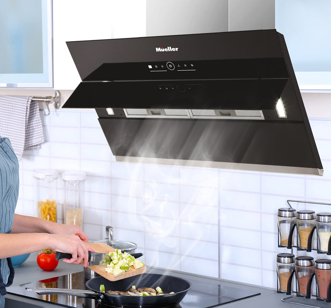 Black Mueller range hood in a kitchen setting with a person cooking.