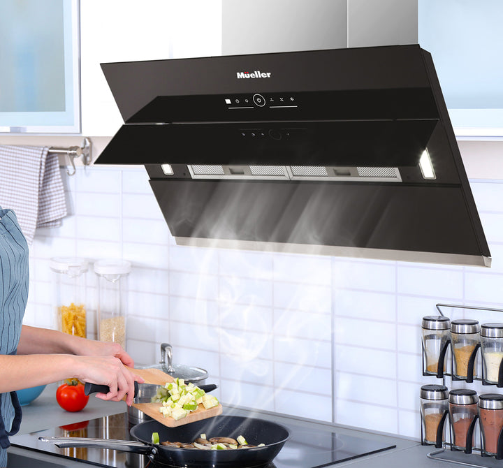 Black Mueller range hood in a kitchen setting with a person cooking.