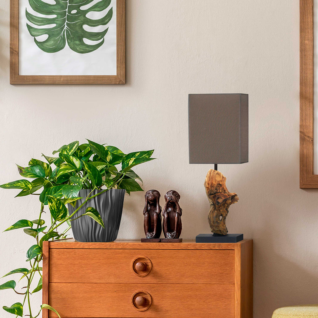 Wooden dresser with a potted plant, lamp, and decorative items against a beige wall.
