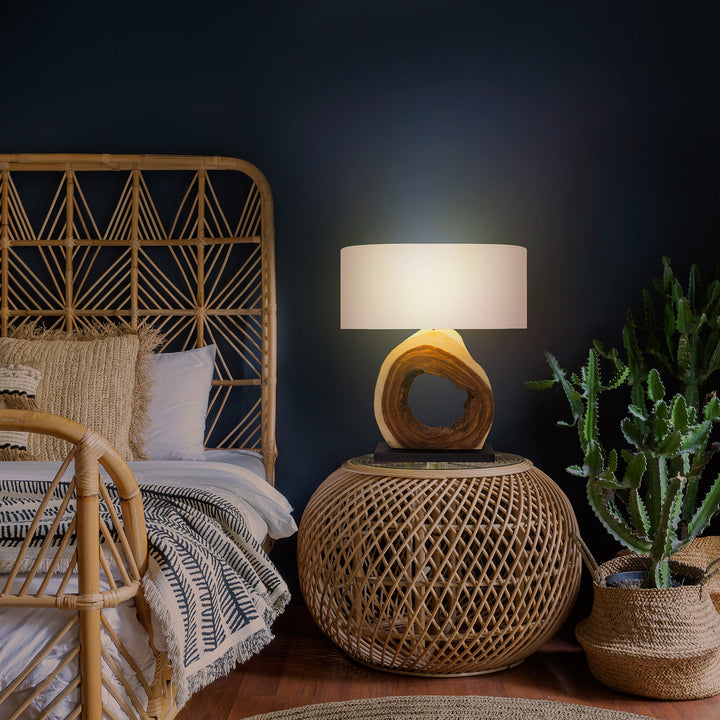 Wicker bed with geometric headboard, lamp, and plant against a dark wall