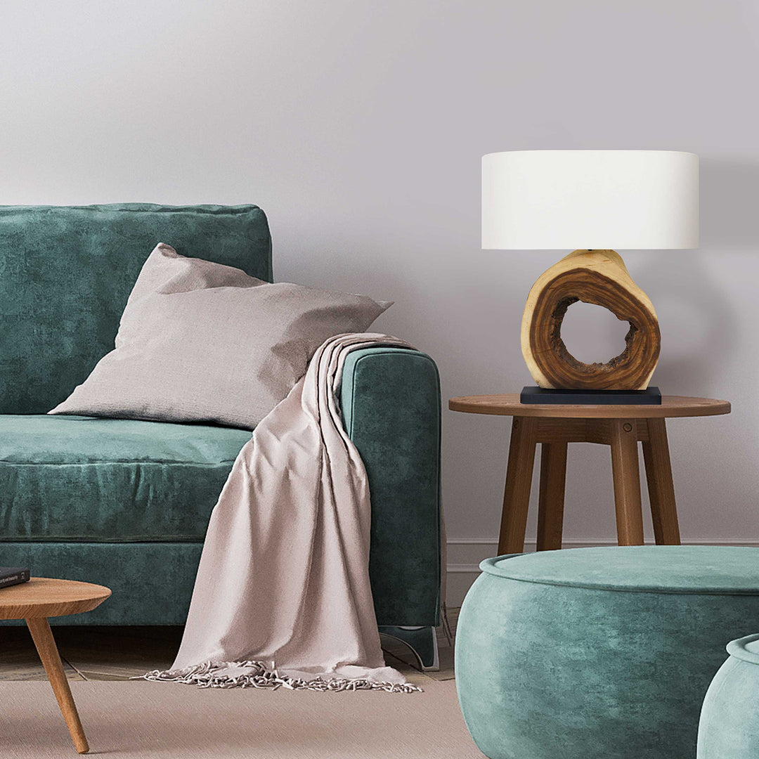 Green sofa with a beige blanket and pillow, wooden side table with lamp, and teal ottoman in a room.